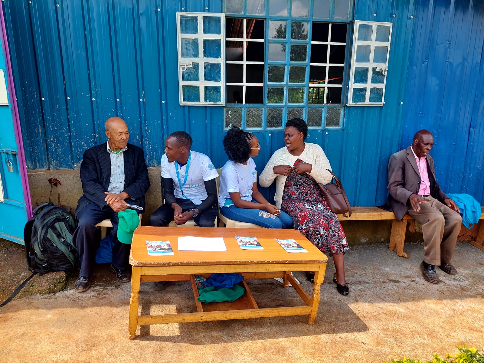 Mental360's team sitting on a bench alongside people from the community. The team is shown wearing team t-shirts in conversation with community folks.