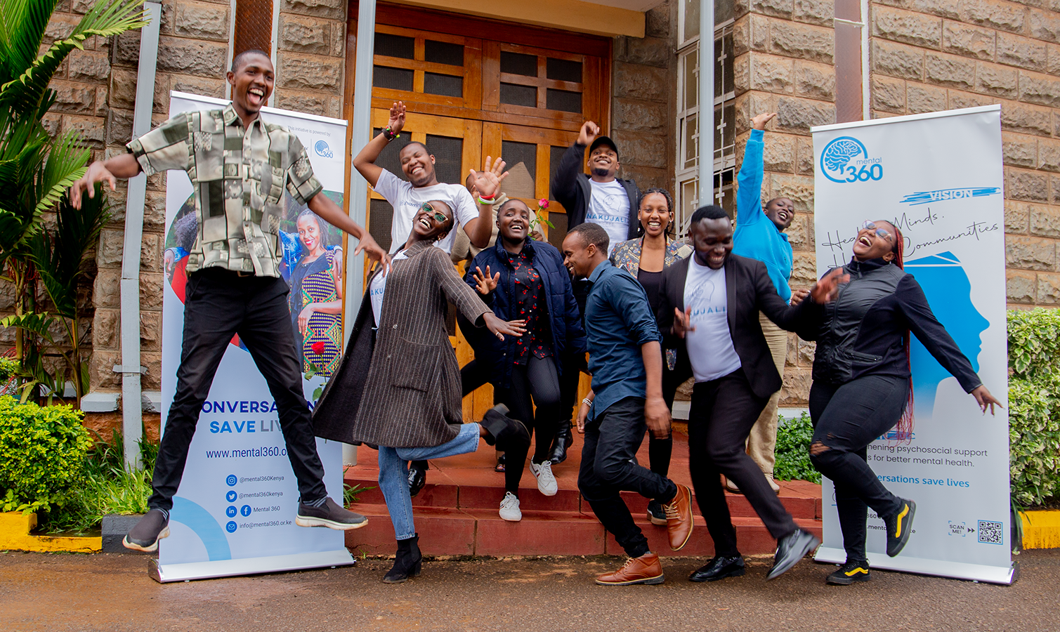 Mental360's team jumping for a photo in front of a building, and in front of the Mental360's banners.